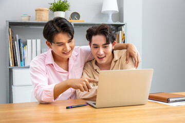 Happy two Asian men gay couple collaborating on laptop at home, working together in a relaxed atmosphere