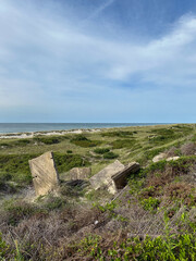 Remains of a WW2 bunker and a view of grass covered sand dunes and the ocean in the Outer Banks