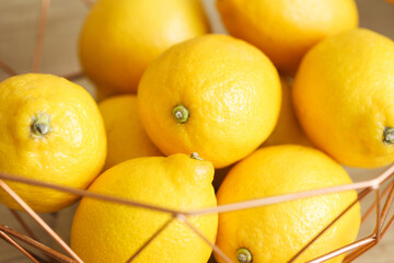 Lemons in a modern metal bowl on a brown wooden table. Stylish fruit display. Home interior design. Rustic kitchen setting. Bunch of lemons. Fruit background. Group of fruits. Close Up macro citrus.