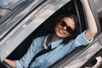 smiling woman with sunglasses sitting in car's driver seat, sunroof open, looking out window,...