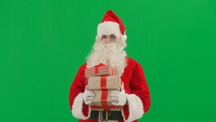 Christmas and New year creative concept. Portrait of man dressed as Santa on chroma key green screen background. Santa Claus in red outfit carrying gift boxes.