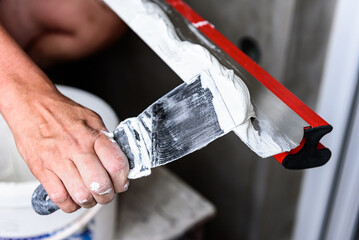 Woman plastering the walls with finishing putty in the room with putty knife or spatula.