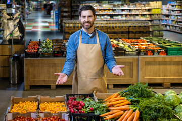 Friendly shopkeeper in grocery store stands next to table filled with fresh organic vegetables. Vibrant display includes carrots, radishes, and tomatoes. Inviting ambiance highlights freshness