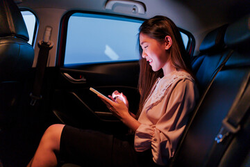 Beautiful asian woman in the passenger back seat of the car, happy smiling, female businesswoman using a mobile smartphone connected to the internet in an automotive transportation vehicle.