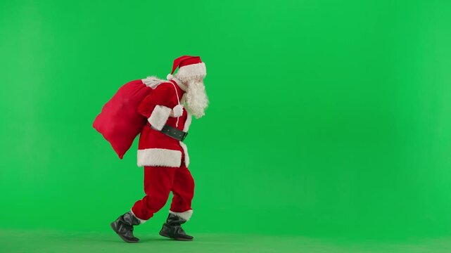 Man in red Santa suit on green background. Santa Claus with sack of presents sneaks on tiptoes and shows gesture secret.