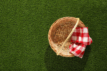 One picnic wicker basket with checkered napkin on green grass, top view. Space for text
