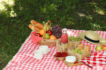 Picnic wicker baskets with delicious food, drink and tableware on checkered blanket outdoors