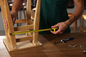Man using tape measure while repairing wooden stool indoors, closeup
