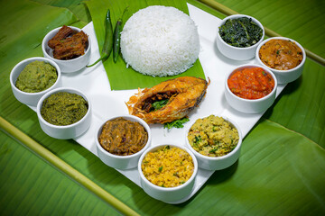 Traditional Bengali dishes such as bhorta, bhaji, fish curry, and vegetable curry are served in white ceramic pots and with Banana leaves.