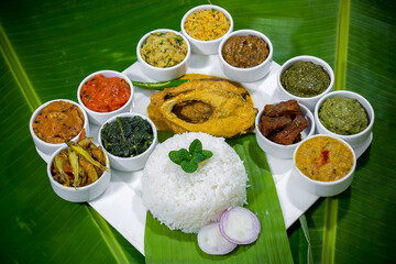 Traditional Bengali dishes such as bhorta, bhaji, fish curry, and vegetable curry are served in white ceramic pots and with Banana leaves.