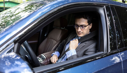 Handsome businessman in black suit fastening belt driving in luxury car. He demonstrating importance of fasten belt rules