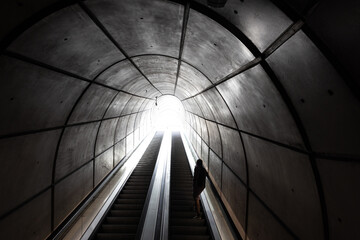 man ascending on escalator inside an urban tunnel, dark, moody - Powered by Adobe