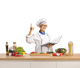 Female chef posing behind a counter with vegetables and holding a cook book