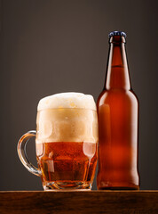 A bottle of beer and a glass of beer on a dark background.
