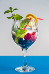 Non-alcoholic cocktail raspberries blueberries lemon and mint in a glass with a straw on a blue background.
