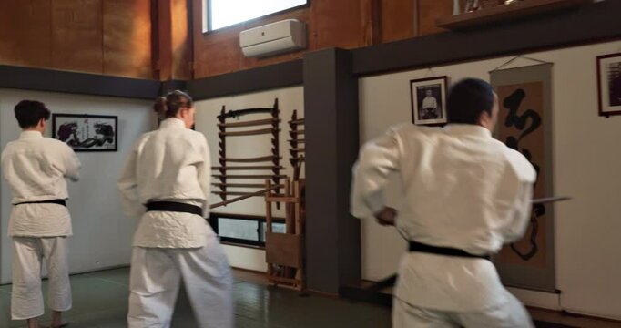 Group of students, stick or learning martial arts in dojo for practice, aikido movement or self defense. Combat, people or training workout for fighting attack or teaching black belt class in Japan
