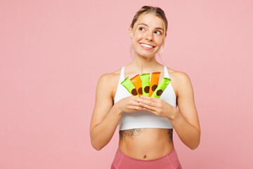 Young fun woman wear white top casual clothes hold in hand energy protein bars look aside on area...