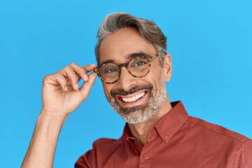 Happy smiling middle aged man, mature confident grey-haired male model wearing shirt holding stylish eyeglasses looking at camera isolated on blue background. Optics eyewear glasses ads. Portrait.
