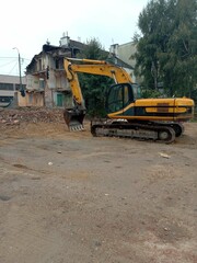 A yellow and black construction machine is parked in front of a building that is being demolished. The machine is a backhoe, and it is surrounded by rubble.