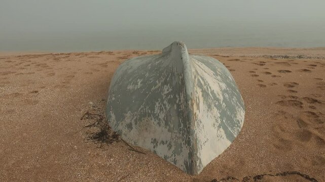 The seashore after a strong winter storm. The fishing boat was washed up on the shore, washed away by sand. Calm after the storm, foggy warm weather