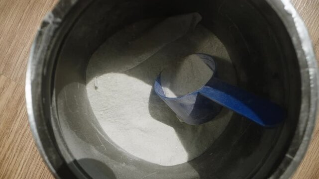 Tossing the blue scoop back into the pre-workout powder jar, deciding against using the supplement. Dolly slider, close up. Slow motion.