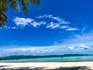 Idyllic view of a sandy beach with palm trees and a sailboat