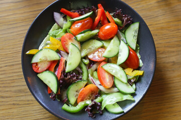 Vinaigrette salad served in a bowl. Mixed vegetables in a fine dining setting with a wooden table. Fresh greens with dressing in a restaurant environment. Healthy lunch background.