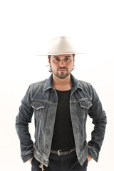 Bearded young man wearing denim jacket and fedora hat over white wall. Vertical.