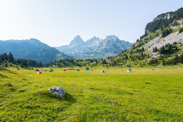 A valley full of tents of hikers camping on a mountain with a view of the peaks in the background