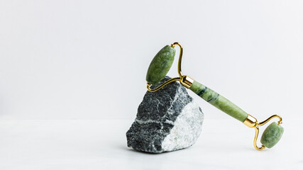 Green jade roller massager for face on white marble.