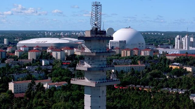 Aerial view of a concrete telecommunications tower overlooking the dense urban landscape of Stockholm, Sweden. The iconic Ericsson Globe and Tele2 arena stand out amidst the cityscape