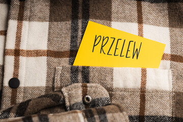  Yellow card with a handwritten inscription "Przelew", protruding from a brown plaid shirt (selective focus), translation: Transfer