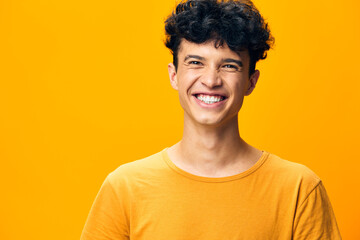 Smiling young man with curly hair in a bright yellow t shirt against a vibrant yellow background...