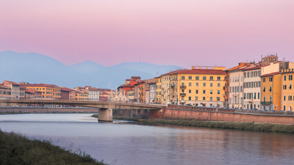 Obraz premium Colorful cityscape of Arno river embankment with buildings, bridge and mountains at sunset, Pisa, Italy