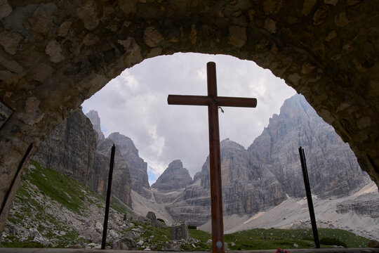 Inside a small chapel near the mountain hut Rifugio Maria e Alberto ai Brentei in Brenta Dolomites. The mountain pass Bocca di Brenta in background. Large cross in foreground.