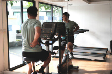 This is a kind of sport injury concept; Asian male athlete sitting on spin bicycle fitness workout and lower leg cramp and backache, Sport man massaging sore muscles during training in fitness gym.