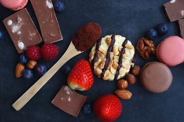 Macarons, chocolate, cookies, berries and various nuts on dark blue background. Top view.
