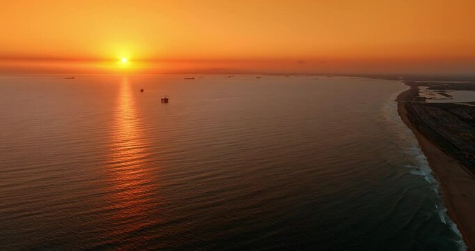 Shore of the Pacific Ocean at sunset. Los Angeles beach from aerial perspective. Orange sky above the horizon over the vast waterscape.