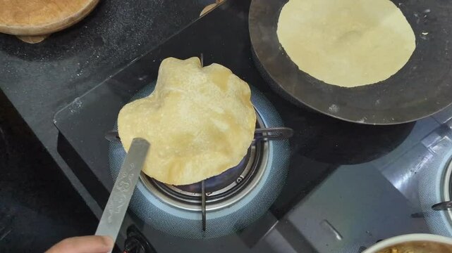 woman's hand cooking a phulka roti over a gas flame on a stove with expert skill, causing it to puff up and expand into a fluffy, delicious flatbread in the kitchen