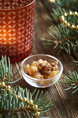 Frankincense resin in a bowl with Christmas candle and decorated spruce tree branches