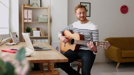 Man learning guitar in online music class with distant teacher on computer from home. Young adult teaching music through laptop. Distance education learning concept