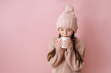 Winter clothes. Portrait of a little girl in a knitted winter hat and sweater with a white mug in her hands