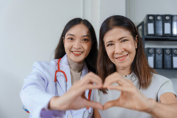 Young doctor and her senior patient are making a heart shape with their hands, expressing care and...