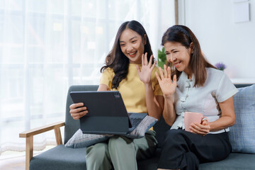 Two asian women happily video call on a sofa, showing the importance of staying connected during...