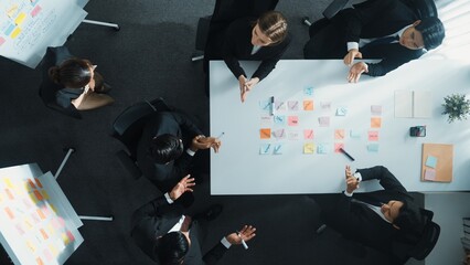 Obraz premium Top down aerial view of business group sharing and brainstorming idea by using sticky notes at meeting room. Investor writing marketing strategy on board while receive note from manager. Directorate.