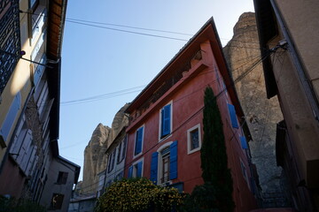 colorful buildings under the Unusual rock formation of Les Mées, France in the village by a yellow flower bush