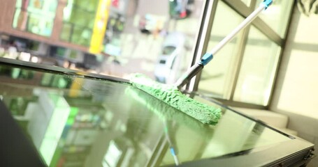 Cleaning a large glass window with a scraper