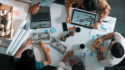 Top aerial view business people brainstorming about building interior at table with house model and laptop displayed house plan while architect engineer drawing and writing at blueprint. Alimentation.