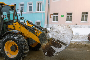 A yellow and black tractor is plowing snow