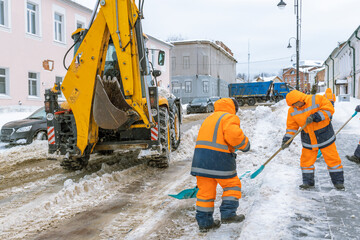 Two men in orange coats are shoveling snow from the street